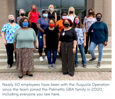 Thirteen women in face masks stand on the front steps of an office building